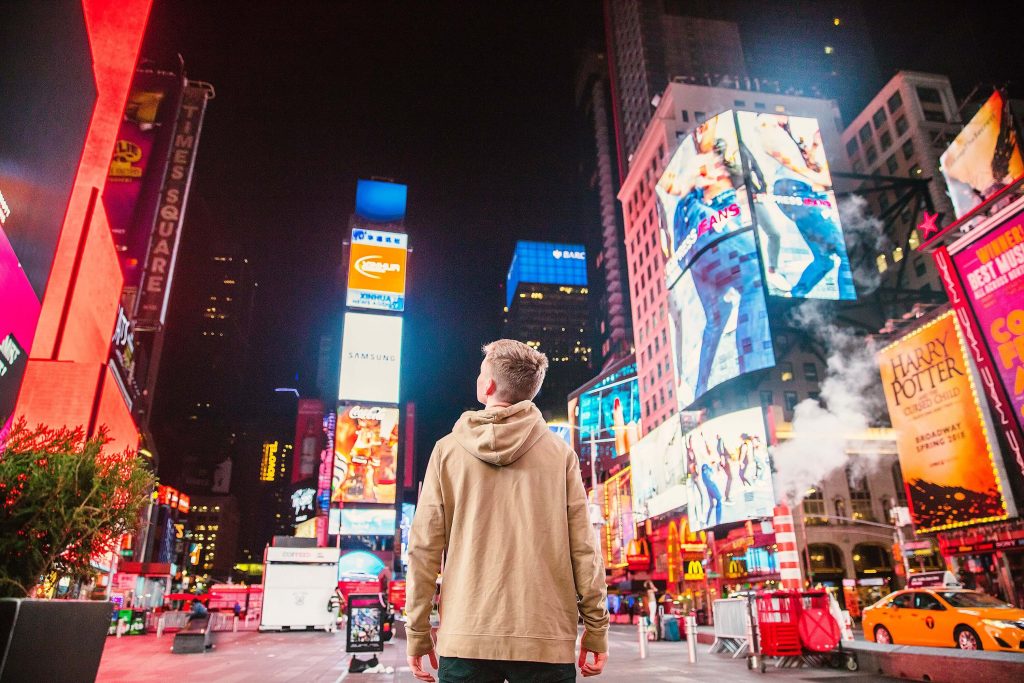 man standing on road in front of high-rise building with ads