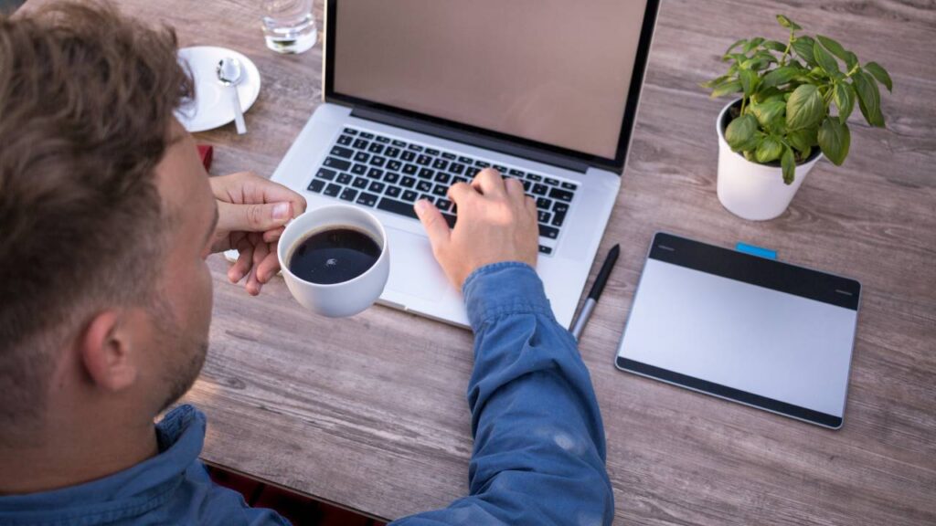 Man having a cup of coffee while working on his laptop